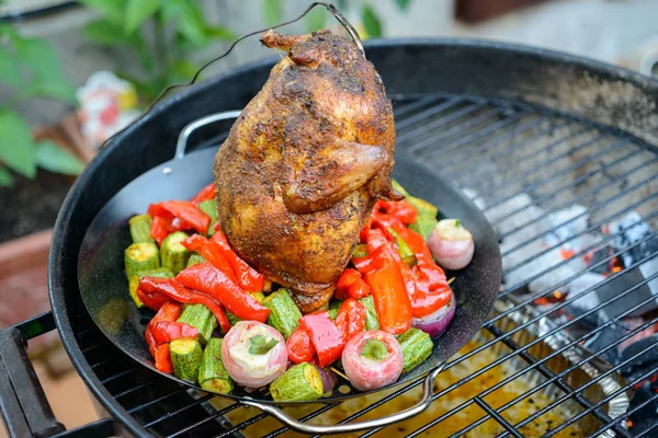 Grilling A Beer Can Chicken in a barbecue, with paprika rub and temperature probe, vegetables in the pan