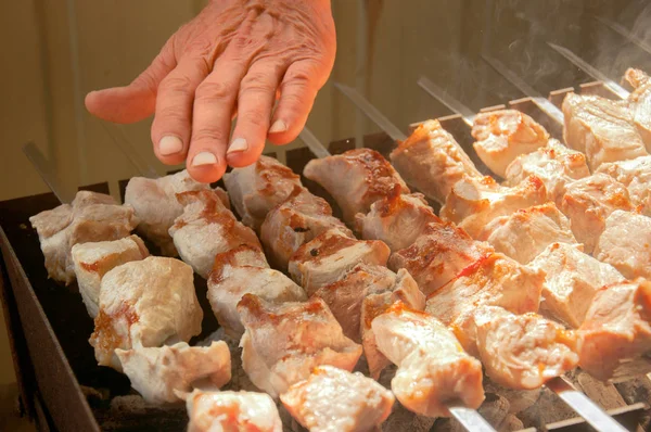Bir adam, barbekülü mangalda elini kontrol eder. Kömür üzerinde şiş kebaplar hazırlanması.