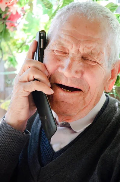 An elderly man is talking on the phone with his daughter. Grandpa communicates with his granddaughter or learns the joyful news. The man is glad to call