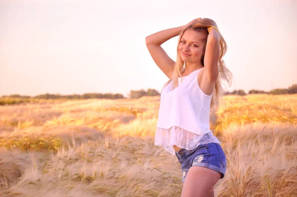 Beautiful girl at sunrise in a wheat field. The girl rejoices that summer has come. A young girl walks the wheat field at dawn and rejoices in the warm morning. A beautiful model walking