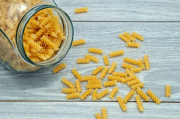 Pasta in a glass jar scattered on a wooden table. A jar of scattered pasta is on the table.