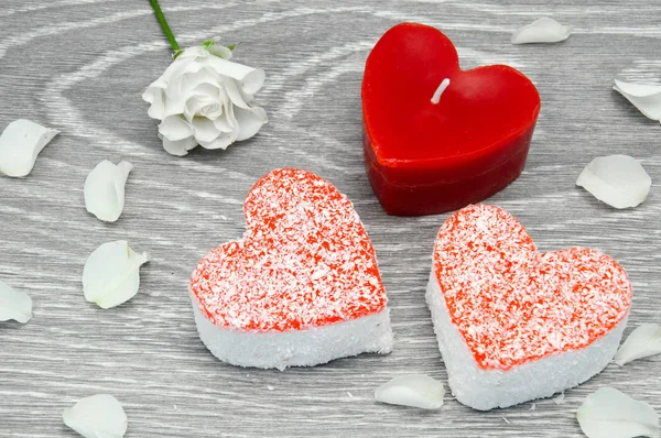 Cakes with a candle in the shape of a heart with a little white rose on a gray background. Red candle in the shape of a heart with rose petals.