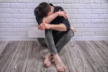 Üzgün adam elinde bir fotoğraf tutuyor. Adam yerde evde oturuyor ve karşılıksız aşk yüzünden üzgün..