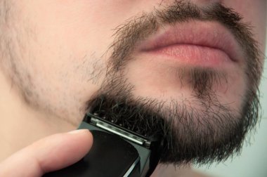 Genç bir adam banyoda tıraş olur. Adam sakalını bir trimer ile tıraş eder. Bakım sakal.