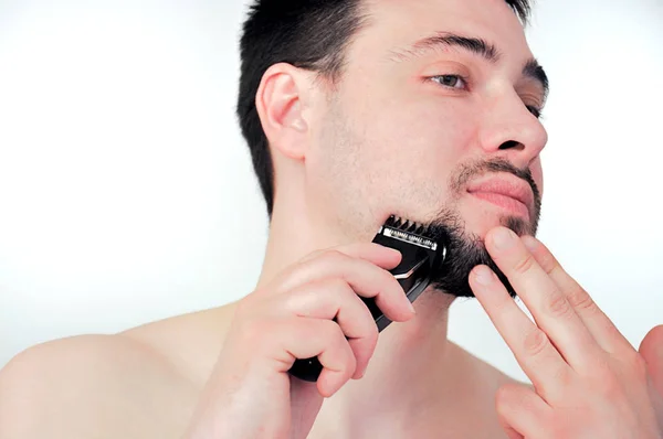 Genç bir adam banyoda tıraş olur. Adam sakalını bir trimer ile tıraş eder. Bakım sakal.