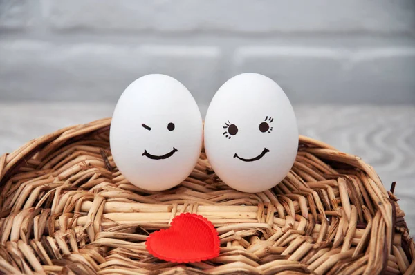 A loving couple of eggs with emoticons and a heart on a wooden basket. Congratulatory card with Easter.