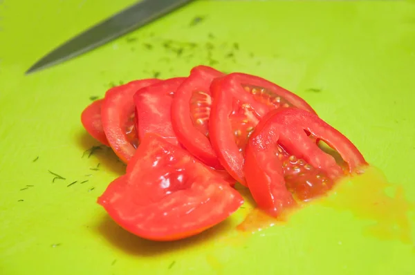 Girl slices a tomato on a green board. Sliced tomato close-up.