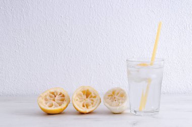 Ahşap bir masada limon ve sıkılmış limon ile su bardağı.