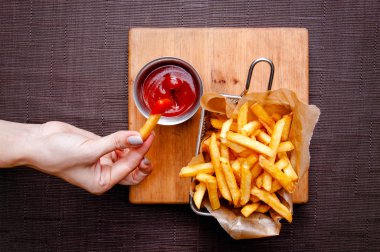 Metal bir kapta patates kızartması ve ahşap bir tahta üzerinde metal bir kase ketçap. Masada soslu patates kızartması.
