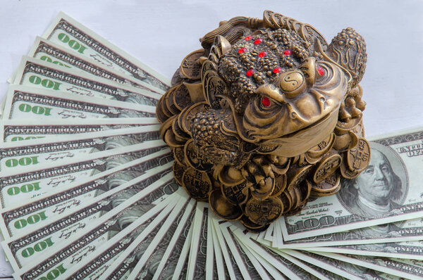 Golden toad with coins sits on money close-up. Toad and dollars. Feng Shui.