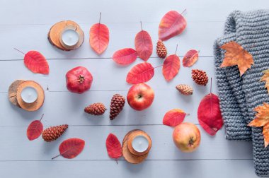 Küçük mumlar, koniler, nar, elmalar, kuru kırmızı yapraklar, beyaz ahşap bir masaya örülmüş gri eşarp. Merhaba sonbahar. Samimi sonbahar arkaplanı.