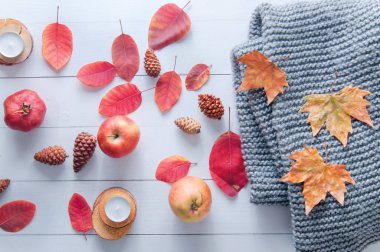 Küçük mumlar, koniler, nar, elmalar, kuru kırmızı yapraklar, beyaz ahşap bir masaya örülmüş gri eşarp. Merhaba sonbahar. Samimi sonbahar arkaplanı.