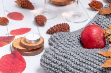 Küçük mumlar, iki bardak gül şarabı, koniler, kuru kırmızı yapraklar, beyaz ahşap bir masaya örülmüş gri bir eşarp. Merhaba, Autumn. Samimi sonbahar arkaplanı.