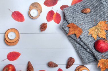 Küçük mumlar, koniler, nar, elmalar, kuru kırmızı yapraklar, beyaz ahşap bir masaya örülmüş gri eşarp. Merhaba sonbahar. Samimi sonbahar arkaplanı.