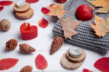 Küçük mumlar, koniler, nar, elmalar, kuru kırmızı yapraklar, beyaz ahşap bir masaya örülmüş gri eşarp. Merhaba sonbahar. Samimi sonbahar arkaplanı.