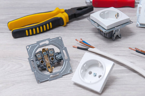 Плоскогубцы, отвертка, провода, розетки крупным планом на сером деревянном полу
.