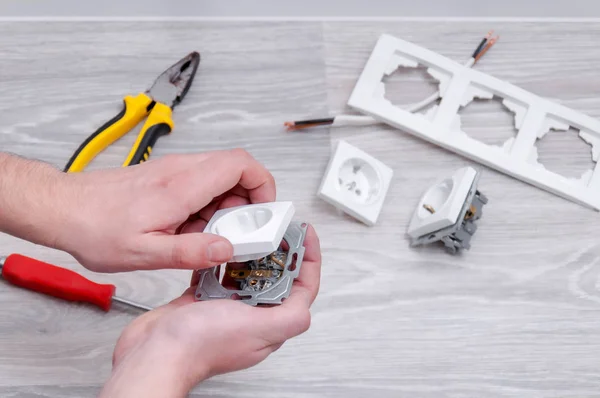 The guy sets the sockets in the room. Repair in the house. Sockets, cable, screwdriver, pliers on a gray wooden floor.