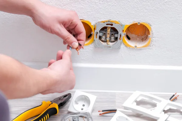 The guy sets the sockets in the room. Repair in the house. Sockets, cable, screwdriver, pliers on a gray wooden floor.