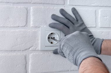 Adam yeni prizler takıyor. Evde tamirat var. Adam tornavidayla prizlerin vidalarını büküyor. Beyaz bir tavan arasında Rosette.