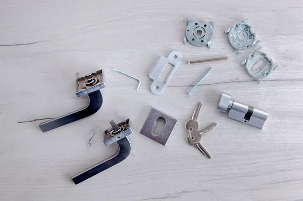 Kilidin çekirdeği, kapı kolları ve anahtarlar arka planda. Evde tamirat var. Kapıya yeni bir kilit takıyorum. Kapı donanımı ve parçalar gri ahşap bir masada..