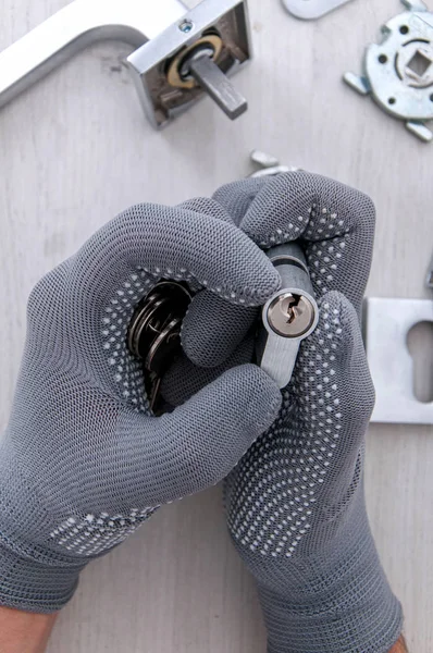 Adam elinde hafif arka planda kapıdan gelen metal bir mat tutacağı tutuyor. Evde tamirat var. Yeni bir kilit ve kapı kolu takılıyor.