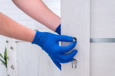 Adam yeni kapı kolları takıyor ve odanın kapısını kilitliyor. Evde tamirat var. Mavi eldivenli adam kapı kollarını tutuyor. Kapı kilidi takılıyor.