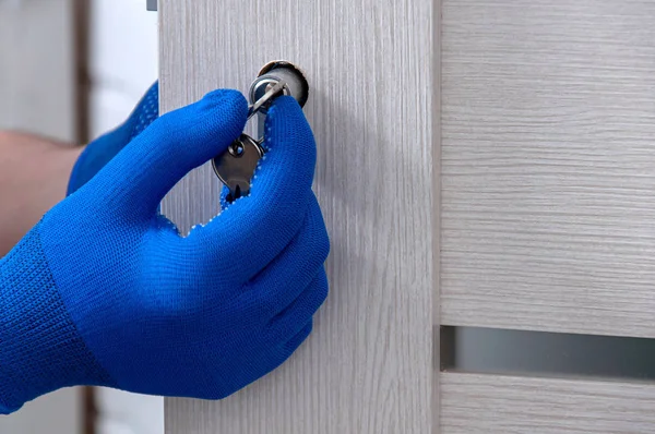 The guy is installing a new door lock in the room. Repair in the house. A guy in blue gloves holds in his hands the core of the door lock. Installing a door lock.