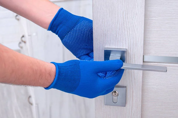 Adam yeni kapı kolları takıyor ve odanın kapısını kilitliyor. Evde tamirat var. Mavi eldivenli adam kapı kollarını tutuyor. Kapı kilidi takılıyor.