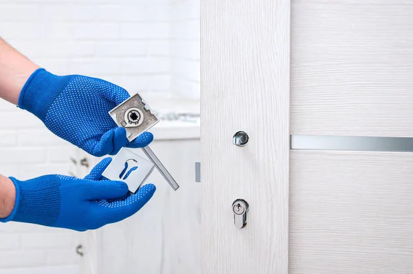 Adam yeni kapı kolları takıyor ve odanın kapısını kilitliyor. Evde tamirat var. Mavi eldivenli adam kapı kollarını tutuyor. Kapı kilidi takılıyor.