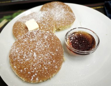 Pudra şekeri, tereyağı ve akçaağaç şurubuyla beyaz tabakta leziz krepler. Amerikan kahvaltısı