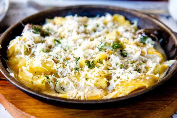Peynirli ve otlu bir tavada lezzetli kızarmış patates. Masada lezzetli yemekler.