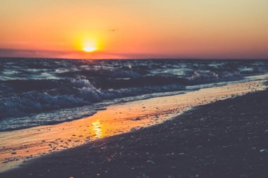 Dalgalar ve güzel turuncu gün batımının yansımasıyla okyanus sahili