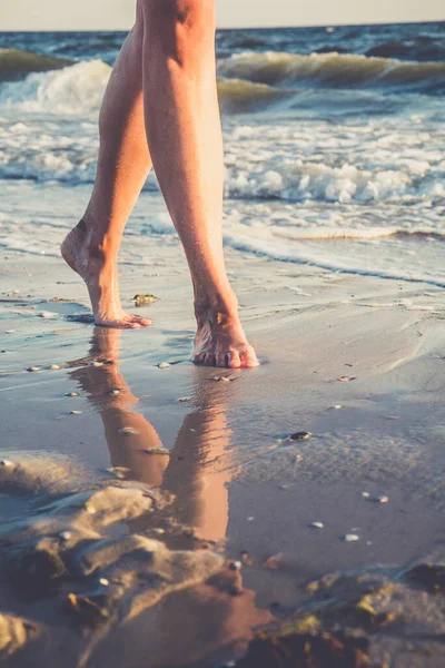 Close up view to female feet. Reflection in the water of barefoot young woman walking on the sand beach. Vertical view