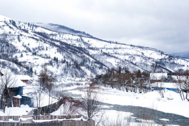 Kış dağı nehri. Bir sürü karlı ve ağaçlı yüksek tepeler.