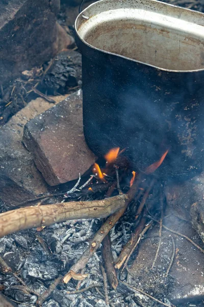 Kamp ateşinin alevlerine konmuş Black Metal kamp tenceresi. Sıcak doğa yürüyüşü ve macera atmosferi.