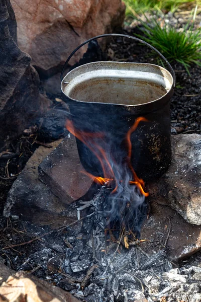 Kamp tenceresi açık havada kamp ateşinde duruyor. Dağlarda yürüyüş yaparken yemek pişirmenin geleneksel yolu..