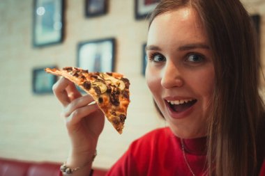 Genç bir kız elinde bir dilim pizza tutuyor..