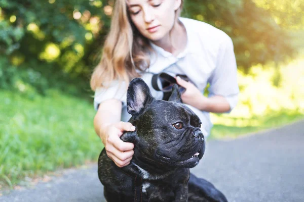 Mooie jonge vrouw die speelt met haar Franse bulldog in een park buiten. Close-up portret van tevreden hond met korte zwarte vacht. Zachte focus op een tevreden hond. — Stockfoto