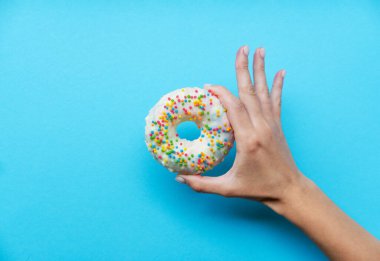 Beyaz kremalı bir çörek. Renkli şekerli bir çöreğin genel manzarası. Mavi arka planda donut tutan bir kadın. Üst manzara, düz yatış. Güzel, diyet konsepti..