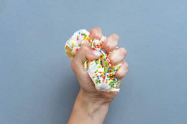 Elin donutu sıkıyor. Beyaz kremalı bir çörek. Renkli şekerli bir çöreğin genel manzarası. Sarı arka planda donut tutan bir kadın. Düz yatıyordu. Diyet kavramı.