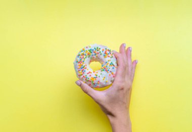 Beyaz kremalı bir çörek. Renkli şekerli bir çöreğin genel manzarası. Sarı arka planda donut tutan bir kadın. Üst manzara, düz yatış. Tatlı, tatlı..