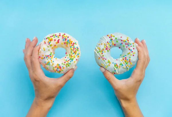 Two donut with white and blue icing. An overhead view of a doughnuts with colored sprinkles. Female hands holding donuts over blue background. Top view. Sweet dessert, diet concept — Stock Photo, Image