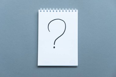 Çizelgesi en tepeden çekilen defter. Spiral defter mavi arka plan. Arkaplanda not defteriyle yazılmış soru işareti. Kopya uzayı ile yatay bileşim.