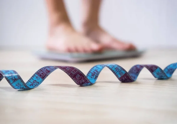 Spiral of a centimeter soft focus close up. Woman with bare feet measures her weight on blurred background. Female legs stand on weigh scales. Healthy lifestyle, slimming and sport concept.