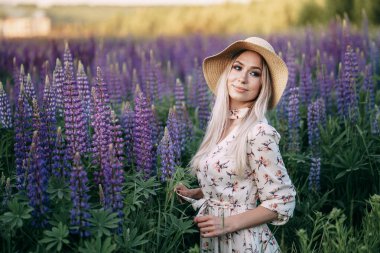 Lupin tarlasında sepeti olan elbiseli sarışın bir kız..