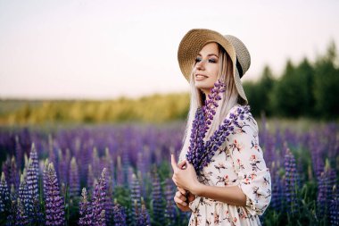 Lupin buketi tutan hasır şapkalı sarışın bir kız..