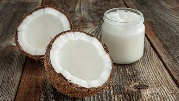 Ahşap bir yüzeyde, kavanozda iki yarım hindistan cevizi ve hindistan cevizi yağı. Sağlıklı gıda kavramı.