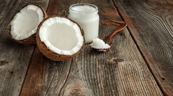 Tahta bir yüzeyde iki yarım hindistan cevizi, kaşık ve hindistan cevizi yağı. Sağlıklı gıda kavramı.