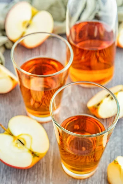 Apple juice in glasses. There are slices of apples and a bottle of juice in the background.