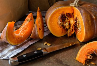 Balkabağıyla hayat devam ediyor. Dilimlenmiş bir balkabağı, iki dilim balkabağı, bir bıçak ve mutfak havlusu var..